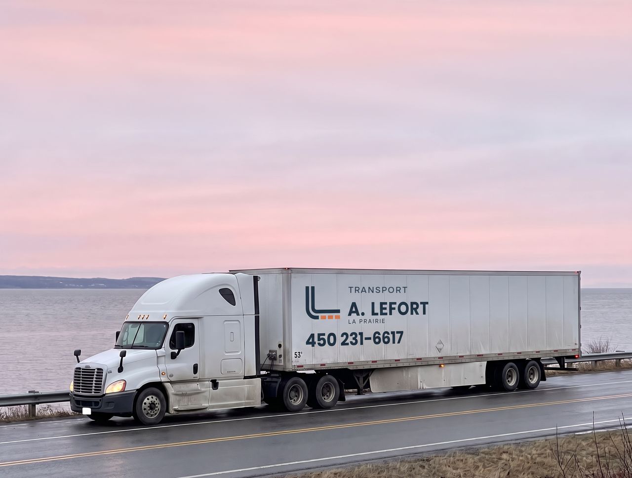 Tracteur routier blanc et remorque aux couleurs d'A. Lefort Transport sur la route, devant le fleuve, au lever du jour